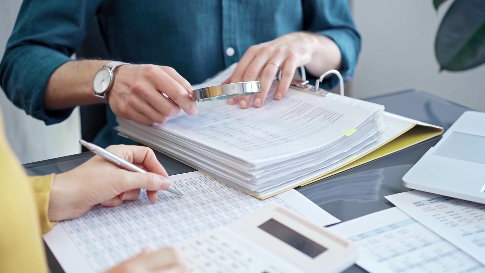 Business colleagues reviewing financial documents and calculating taxes. Auditor inspecting financial reports with magnifying glass. Business audit, taxes and forensic accounting concept