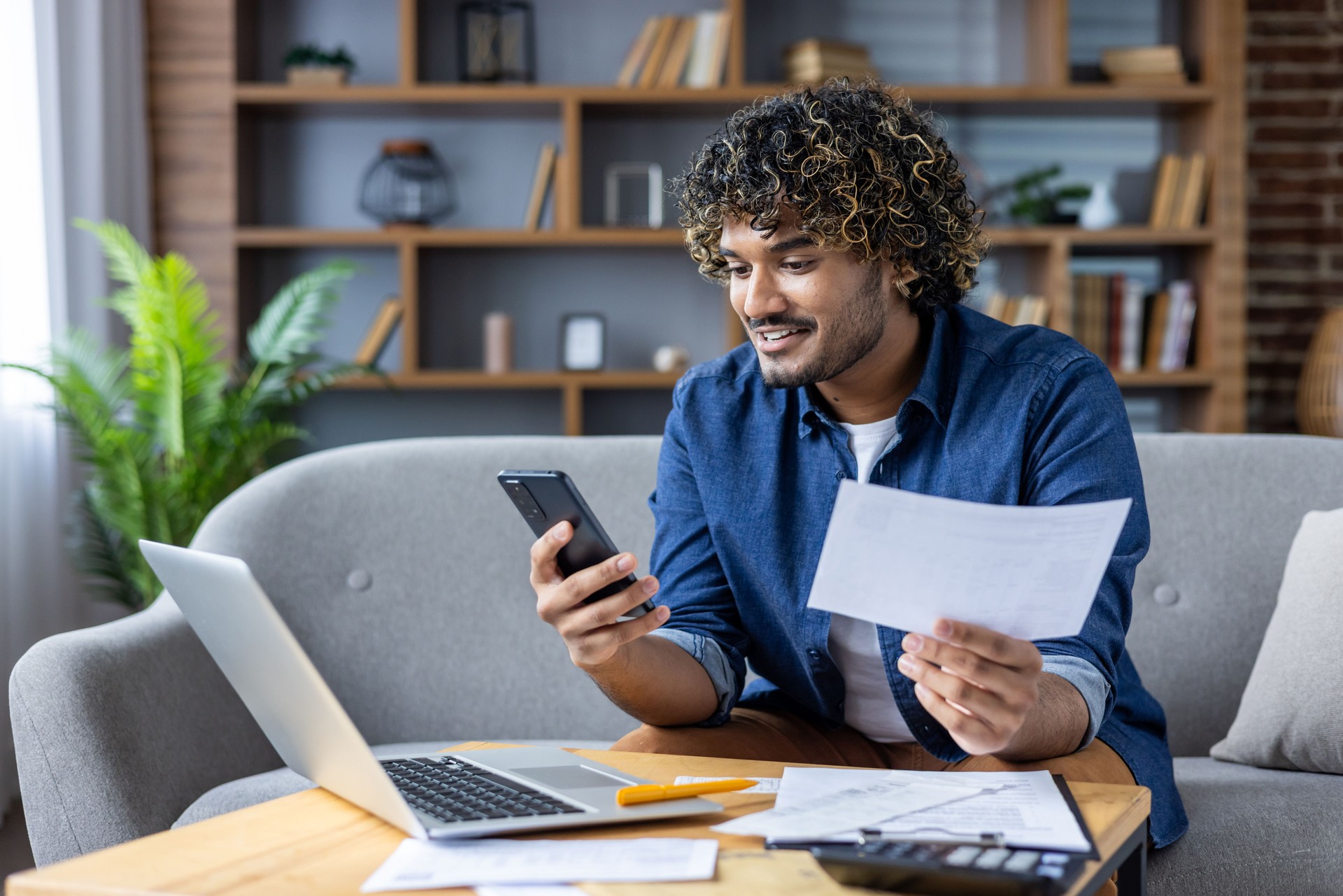 Happy man using smartphone and laptop for online bill payment at home